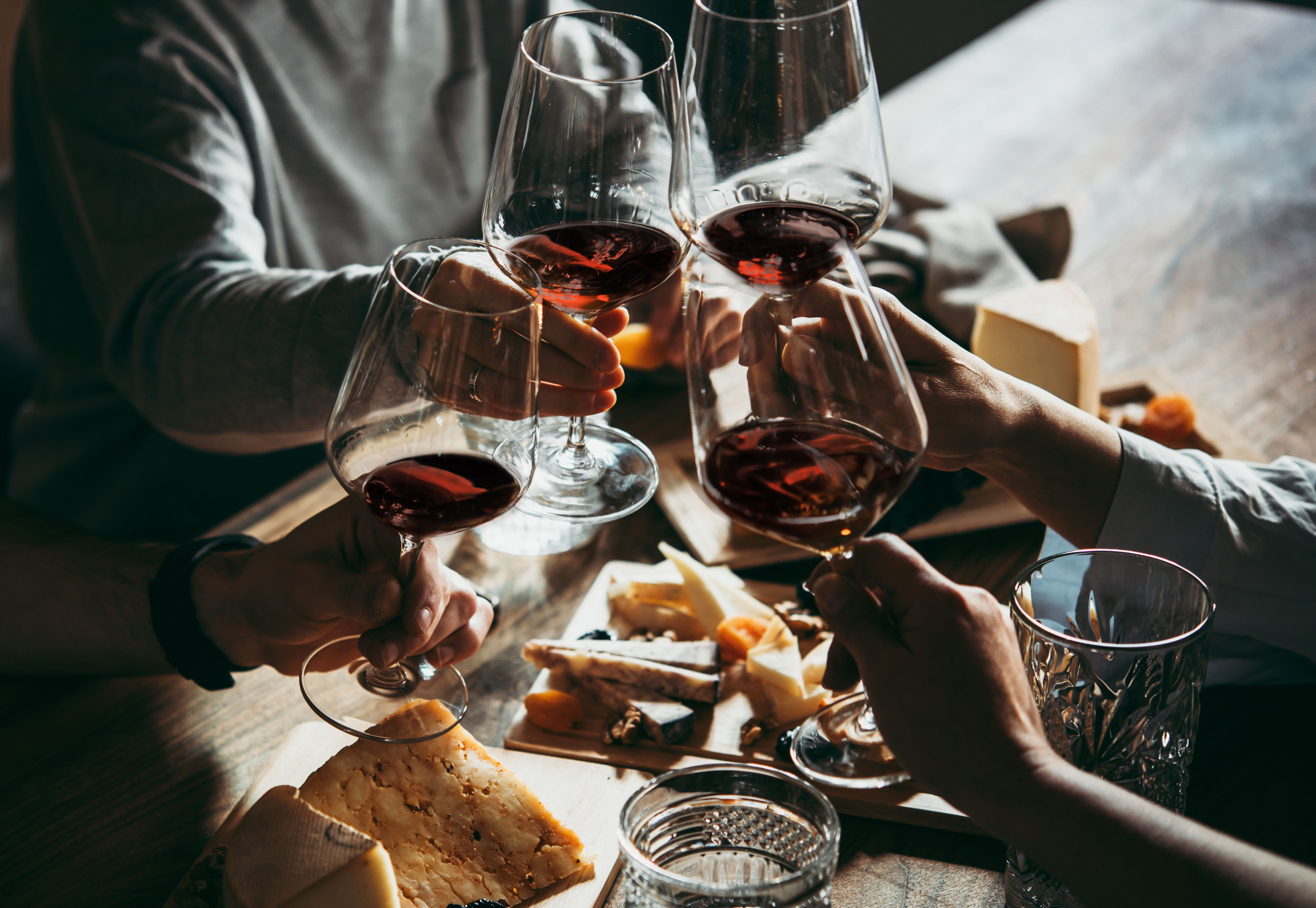 Rotwein Anstoßen mit Rotweingläsern an einem Tisch mit Käse und Brot