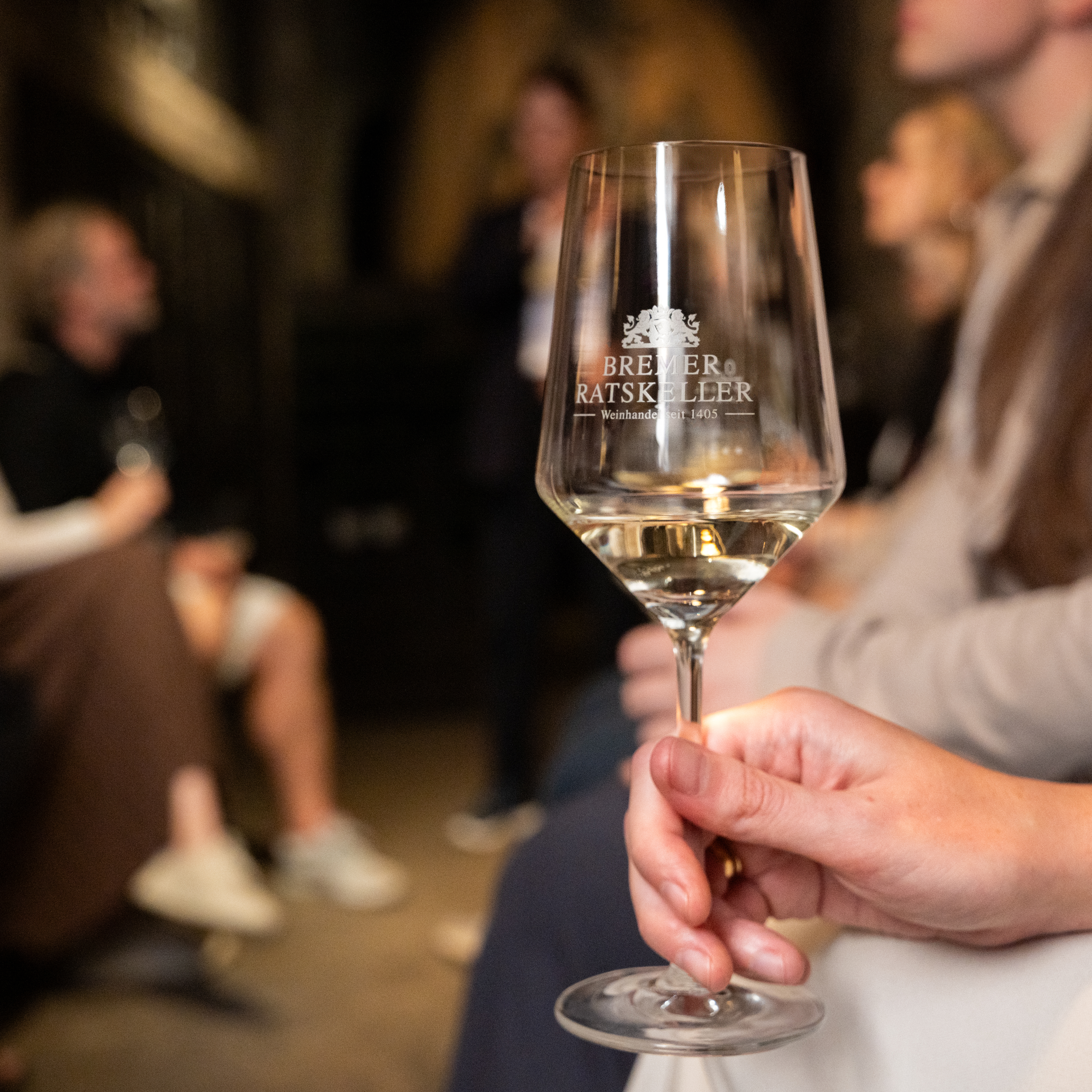 Eine Gruppe Menschen im Ratskeller. Eine Hand hält ein Weinglas
