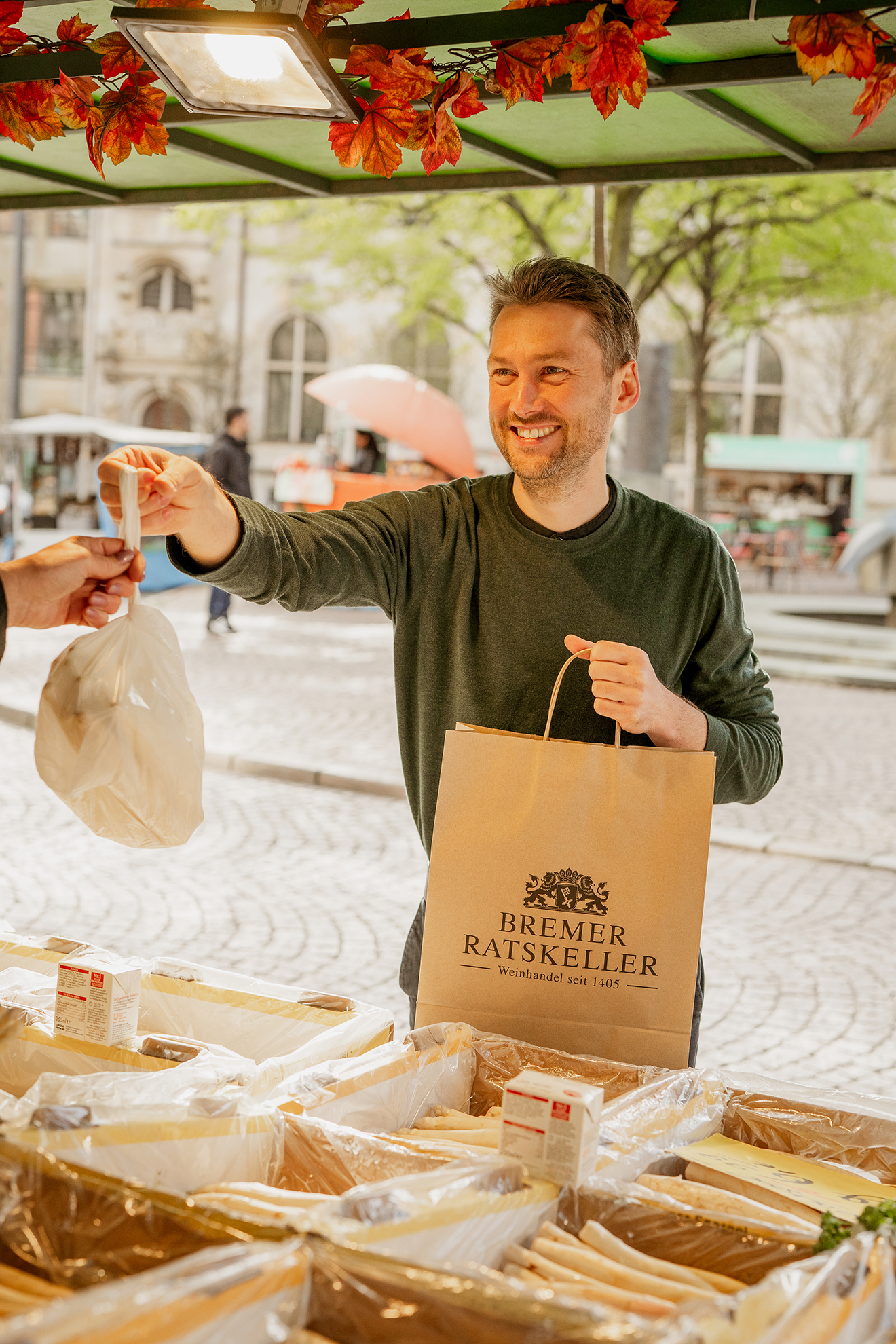 Ratskellermeister Frederik Janus kauf Spargel auf dem Wochenmarkt mit Bremer Ratskeller Einkaufstüte