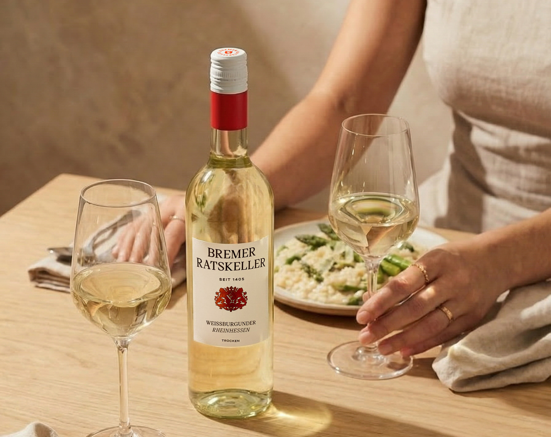 Gedeckter Tisch mit Risotto und grünem Spargel. Einer Flasche Bremer Ratskeller Spargelwein und zwei Gläsern