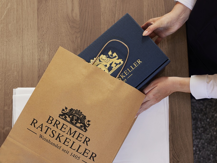 Eine Geschenkverpackung vom Bremer Ratskeller wird in eine Tragetasche verpackt