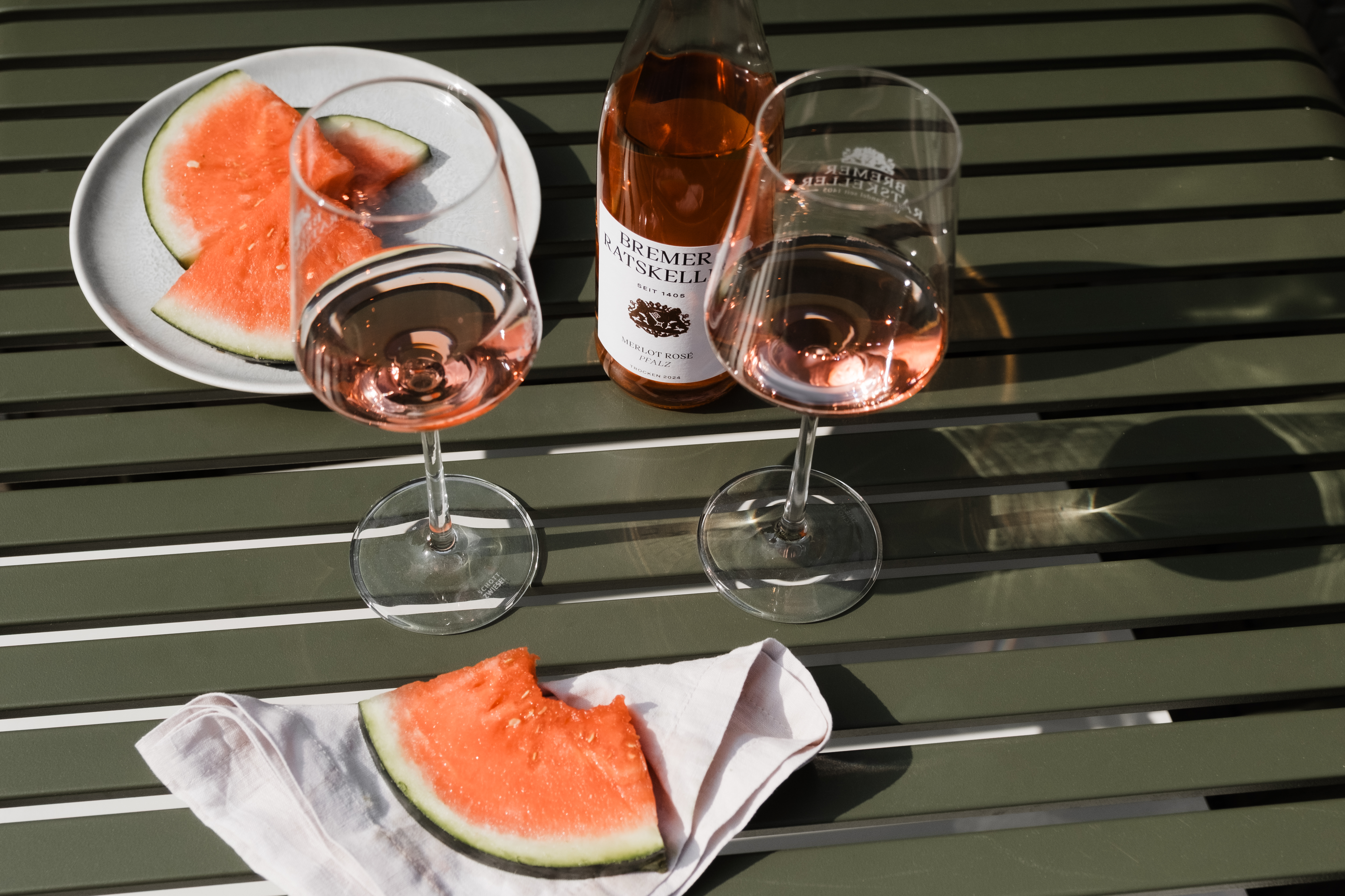 Wassermelonen und Rosé in zwei Weingläsern mit einer Weinflasche vom Bremer Ratskeller auf einem grünen Gartentisch
